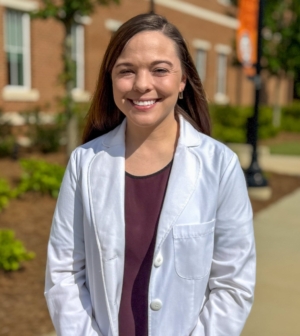 Dr. Jenna Bloemer standing outside of the college of pharmacy in her white coat