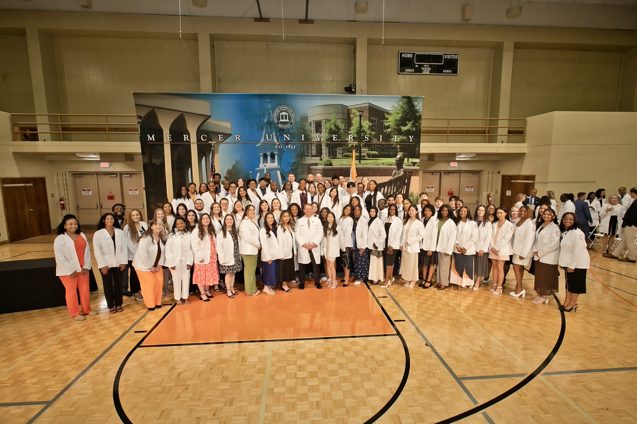 A group photo of the Class of 2029 in the Sheffield Gym on the Mercer Atlanta campus. A Mercer university campus backdrop is behind the students.